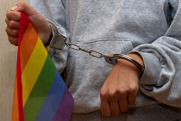 Girl handcuffed, holding LGBT flag. Concept: prohibition and persecution, restriction of freedom.