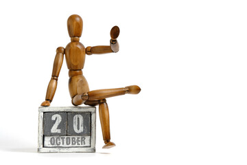 October 20, wooden calendar with mannequin sitting on it on white background. Calendar date.