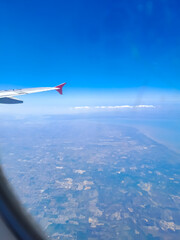 Fototapeta premium Airplane wing with clear blue sky and residential area behind, taken from passenger window