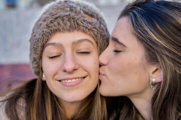 Obraz premium young teenager kissing her friend or sister with affection and emotion. woman kissing her best friend.