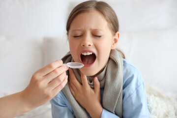 Ill little girl taking cough syrup in bedroom, closeup