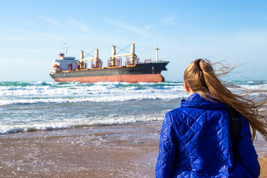 A woman at sea looks at a stranded cargo ship that was thrown out during a storm.