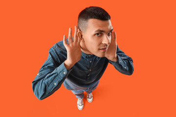 Young man with hearing problem on orange background