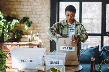 Young African American woman is doing garbage waste sorting at home. Concept of sustainable...