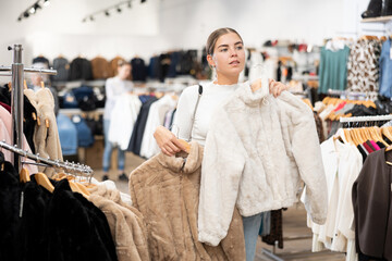 Young cheerful girl demonstrates fur coat in a clothing boutique