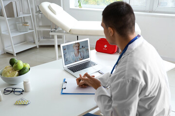 Male doctor video chatting with patient on laptop in office