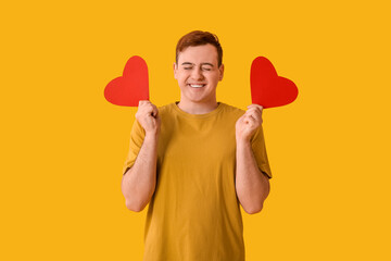 Happy young man with red paper hearts on yellow background