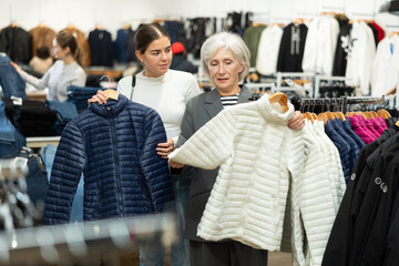 Glad mature female customer holding a hanger with white jacket in retail outlet