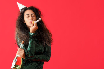 Beautiful young African-American woman with party whistle and bottle of champagne celebrating Birthday on red background - obrazy, fototapety, plakaty