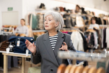 Pleased mature woman watching excitedly large stock of clothes in retail outlet