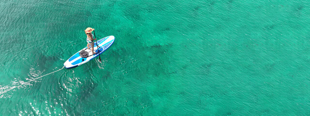 Aerial drone ultra wide panoramic photo of young unidentified woman practising paddle board or SUP...