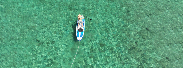Aerial drone ultra wide panoramic photo of young unidentified woman practising paddle board or SUP...