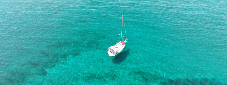 Aerial drone ultra wide panoramic photo of beautiful sail boat with white sails anchored in tropical exotic bay with emerald clear sea