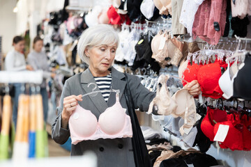 Mature woman selecting new bra in lingerie department underwear shop - obrazy, fototapety, plakaty