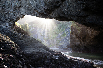 Sunbeams streaming through an arch at Secret Beach in the Samuel H. Boardman Scenic Corridor on...