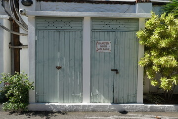 Small building with grey wooden door and shield with text, dander high voltage. Behind the door is...