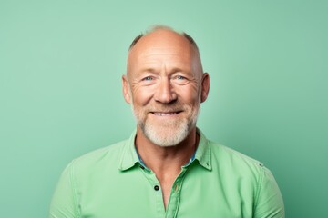 Portrait of a smiling senior man in a green shirt on a green background.