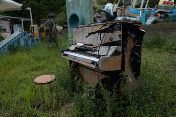 Broken piano with a chair located outdoors in the abandoned amusement park with a rusty carousel in the background