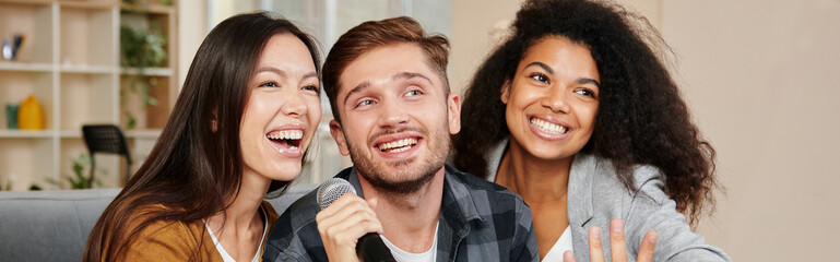 Karaoke singers. Three smiling friends looking happy while playing karaoke at home, singing with microphone, sitting on the couch in the modern apartment