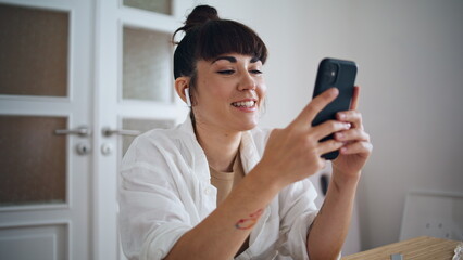 Smiling artist holding smartphone home close up. Earphones woman listening music