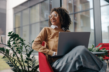 Pretty female freelancer working on laptop while sitting on modern coworking background