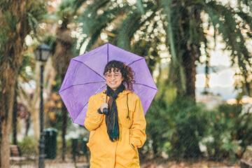 Rainfall season, cold winter weather. Latin mid adult woman smile on raincoat and umbrella