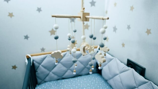Cozy empty bed with soft sides for a baby boy. Nursery crib mobile of natural materials is hanging above the cot.