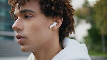 Serious model face talking earphones at street portrait. Curly guy using earbuds