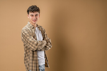 Portrait of one caucasian man 20 years old looking to the camera in front of almond color studio background smiling wearing casual shirt copy space