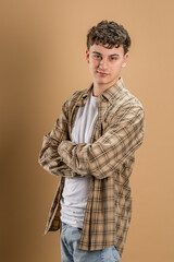 Portrait of one caucasian man 20 years old looking to the camera in front of almond color studio background wearing casual shirt copy space