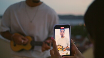 Girl hands recording man guitar playing video sunset terrace. Guy singing song