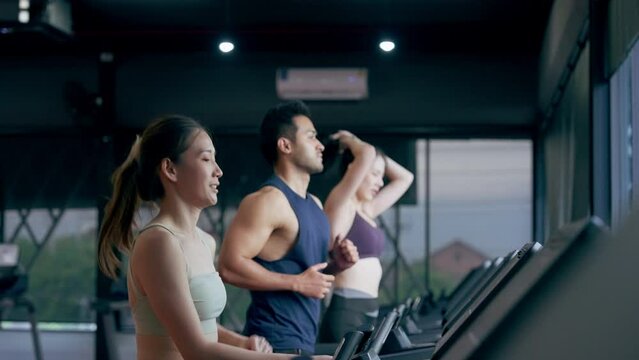 Fit young woman and man running on a treadmill during a workout class at fitness gym