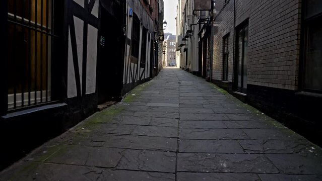 Liverpool, UK - May 20 2023: POV handheld walking down a dark, shadowy stone alleyway toward the bright opening ahead