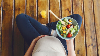 View a pregnant womanholding a bowl with fresh salad, enjoyinghealthy lifestyle during her pregnancy