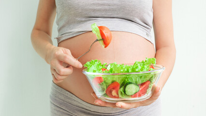 View a pregnant womanholding a bowl with fresh salad, enjoyinghealthy lifestyle during her pregnancy