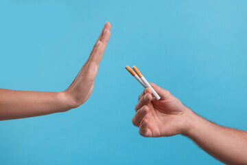 Stop smoking concept. Woman refusing cigarettes on light blue background, closeup