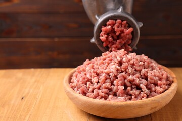 Manual meat grinder with beef mince on wooden table, closeup. Space for text