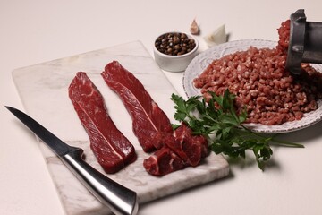 Manual meat grinder with beef, peppercorns and parsley on white table