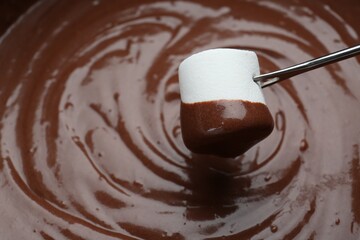 Marshmallow with melted chocolate on fork above fondue, closeup. Space for text