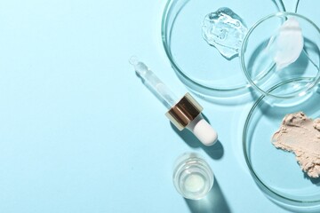 Bottle of cosmetic serum and petri dishes with samples on light blue background, flat lay. Space...