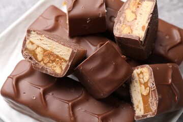 Tasty chocolate bars with nougat, caramel and nuts on plate, closeup