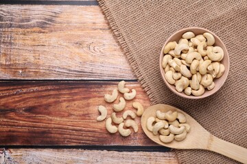 Tasty cashew nuts in bowl and spoon on wooden table, flat lay. Space for text