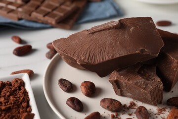 Pieces of tasty milk chocolate and cocoa beans on white table, closeup