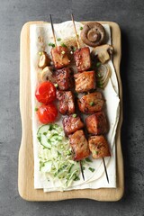 Delicious shish kebabs with vegetables and lavash on grey table, top view