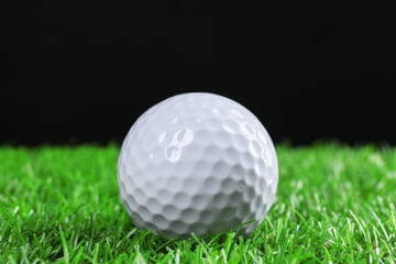Golf ball on green grass against black background, closeup