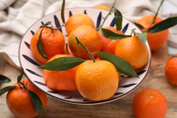 Fresh ripe tangerines with green leaves in bowl on wooden table, closeup