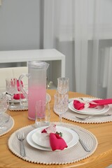 Color accent table setting. Glasses, plates, jug of beverage and pink napkins in dining room