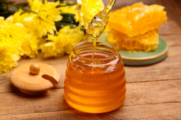 Natural honey in glass jar and dipper on wooden table under sunlight