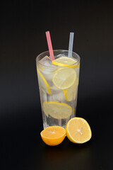 A tall glass of refreshing lemonade with ice and citrus pieces on a black background.