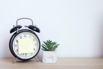 Alarm clock and sticky paper with text space near succulent on wooden table  